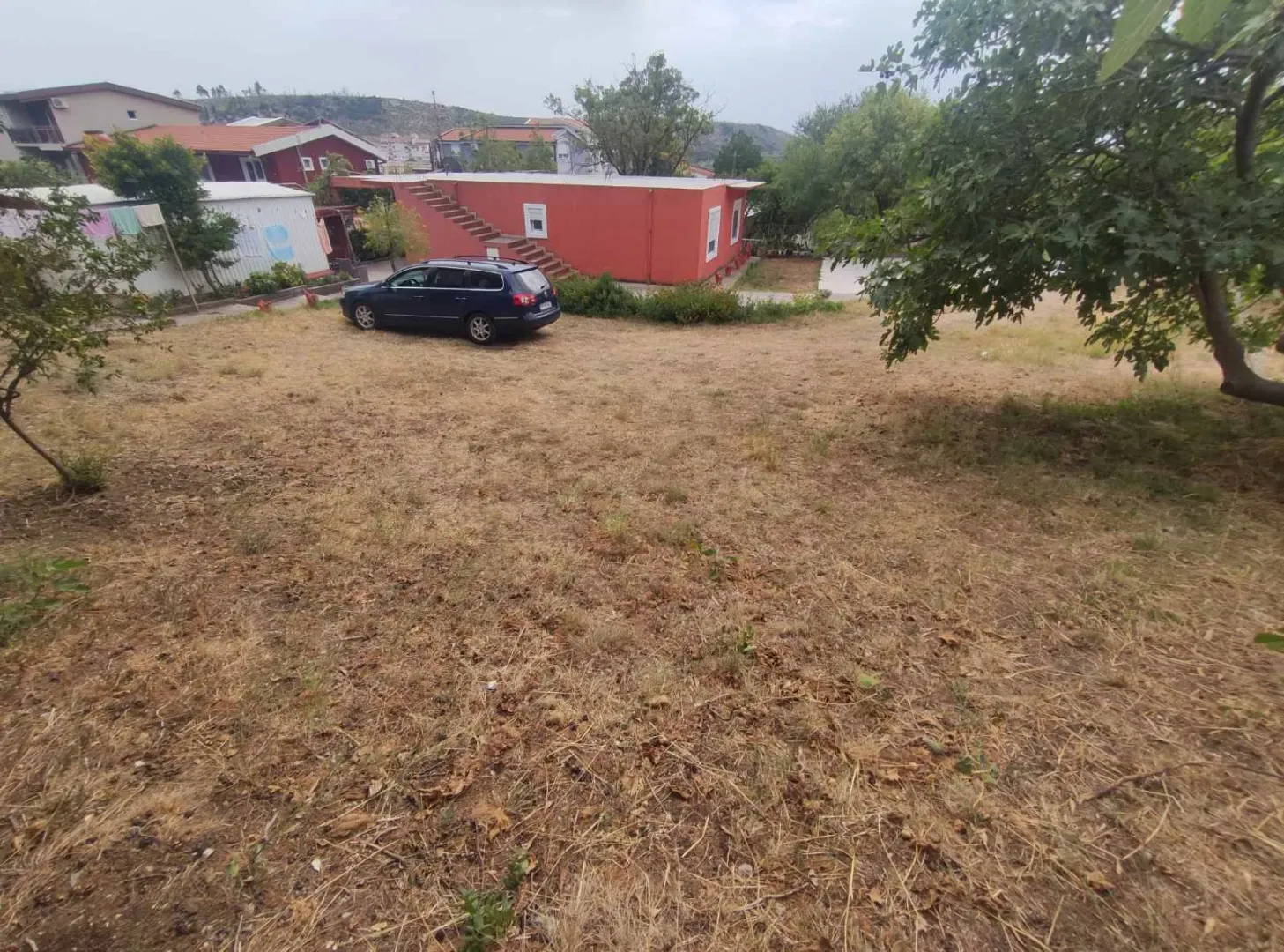 Dvorište kuće sa travnjakom i parkiranim autom.