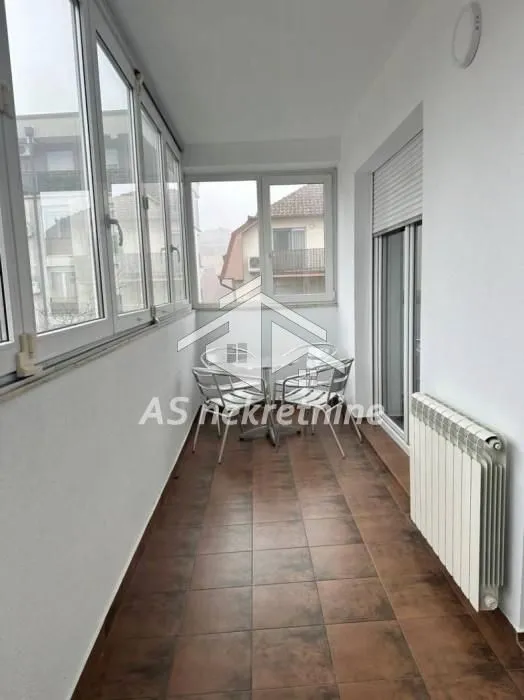 Zastakljeni balkon sa stolom i stolicama.