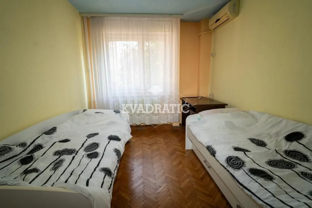 Spavaća soba sa dva kreveta i prozorom sa belim zavesama.
