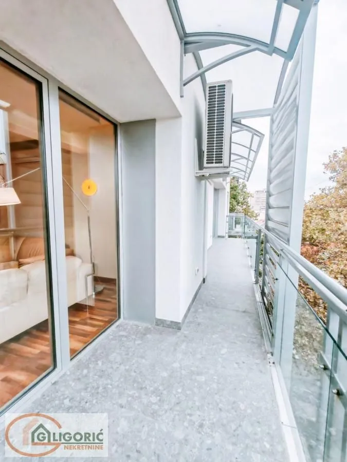 Long covered balcony with glass railing and air conditioning outdoor unit.