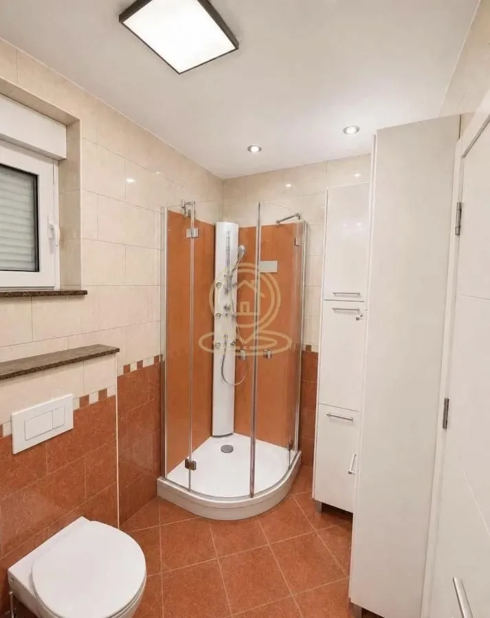 Kupatilo opremljeno tuš kabinom, WC šoljom i belim ormarićima.