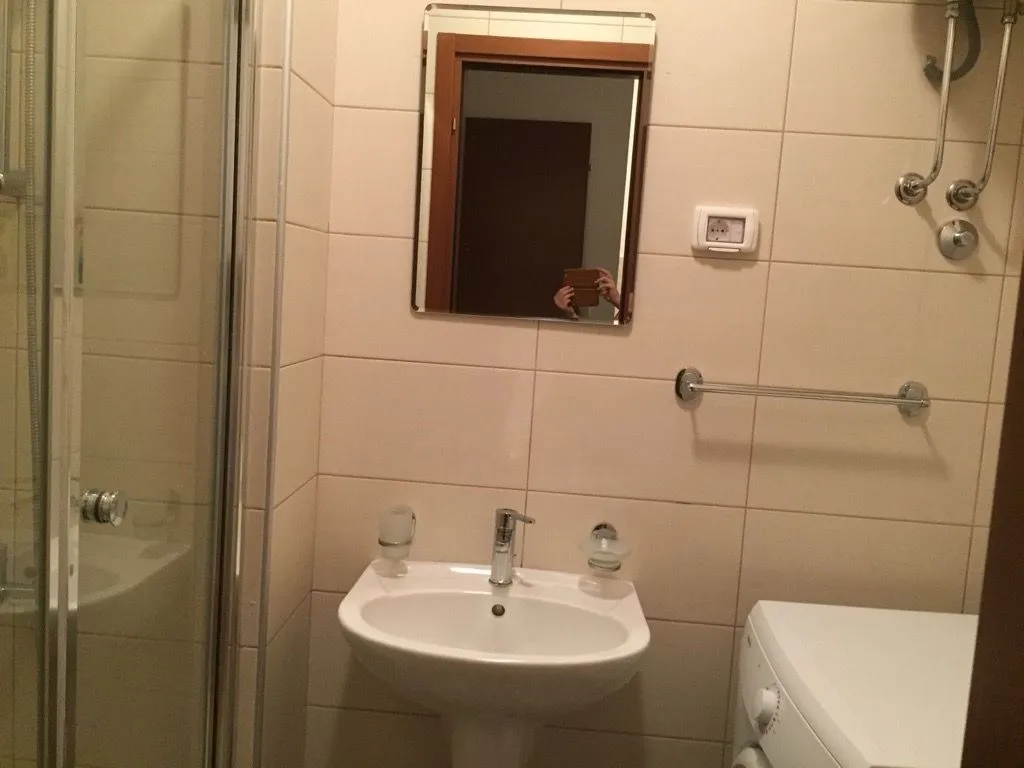 Manje kupatilo sa umivaonikom, tuš kabinom i keramičkim pločicama.