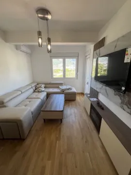Uređena dnevna soba sa ugaonom garniturom, drvenim stočićem i televizorom na zidu. - image 10