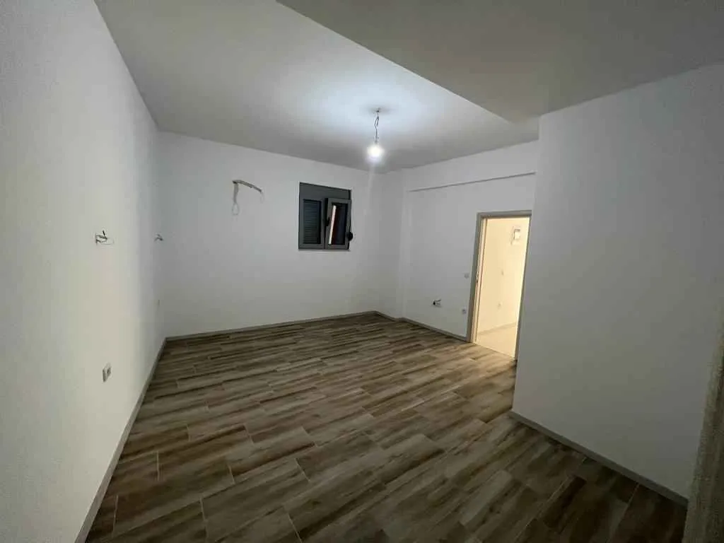 Prazna, prostrana soba sa svijetlim zidovima i podom u dezenu drveta.