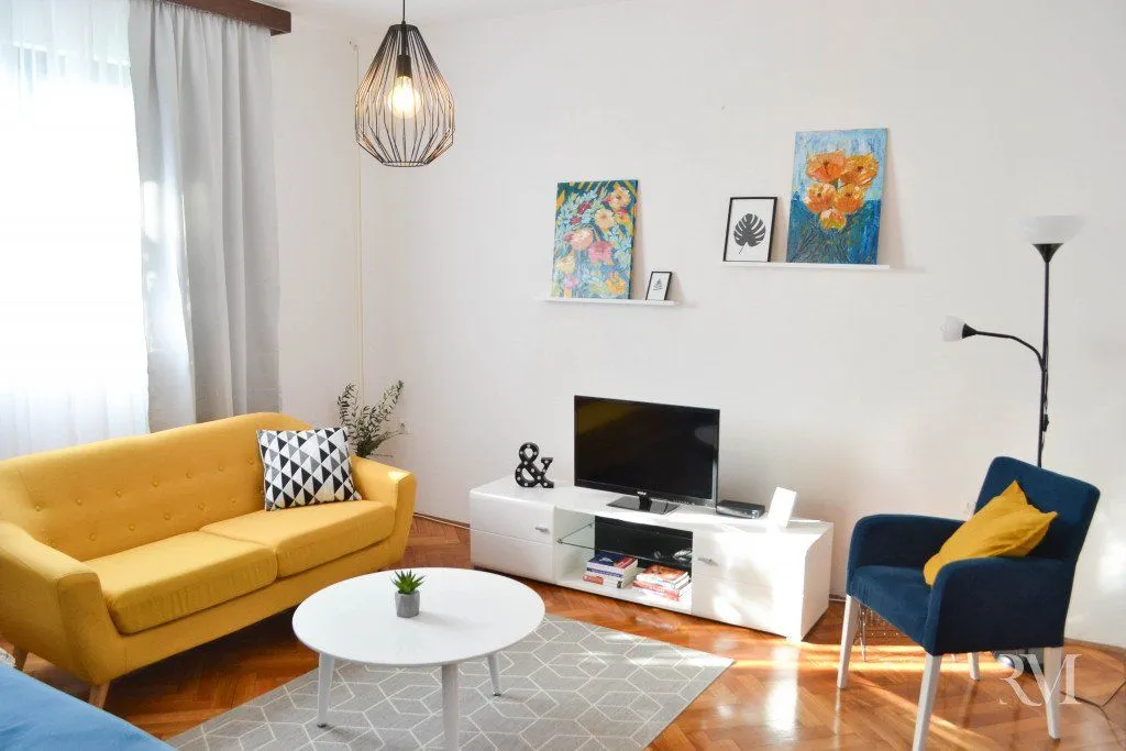 Svijetao dnevni boravak sa žutim dvosjedom, plavom foteljom i modernim namještajem.