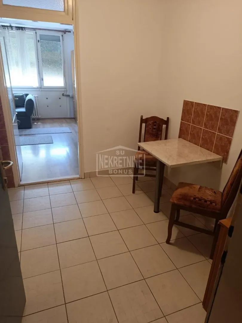 Manja kuhinja sa trpezarijskim stolom i stolicama i pogledom na susednu prostoriju.