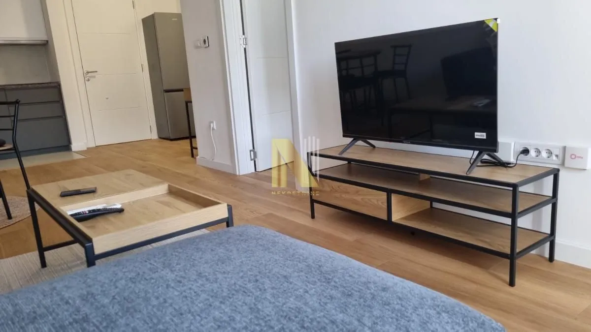 Dnevna soba sa televizorom, stočićem i sofom, sa pogledom na kuhinju.