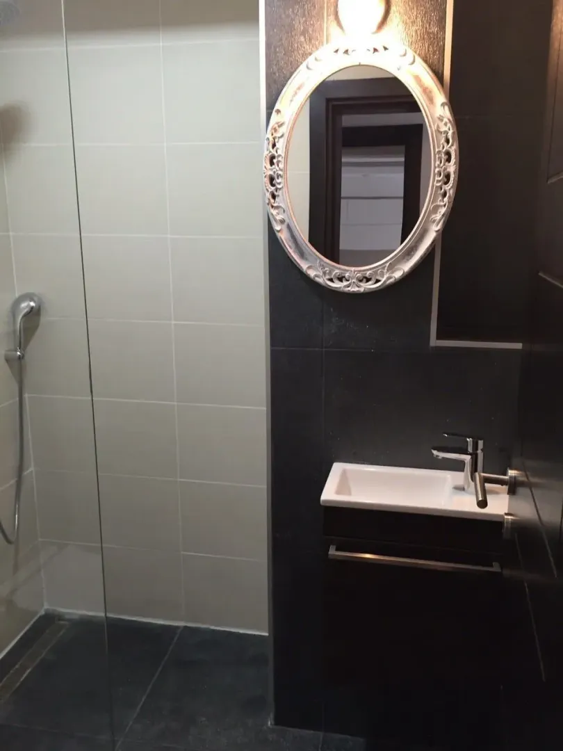 Modern bathroom featuring a shower cabin, small sink, and an ornate oval mirror.