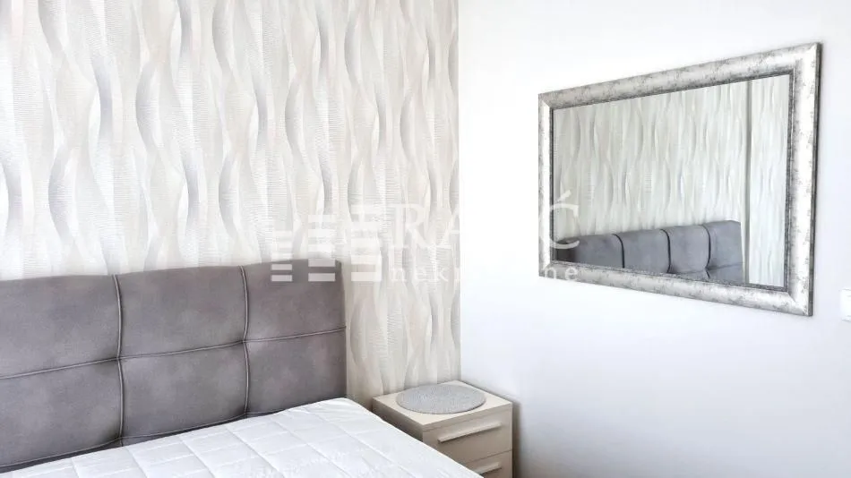 Furnished bedroom with a double bed, wallpaper, and a wall mirror.