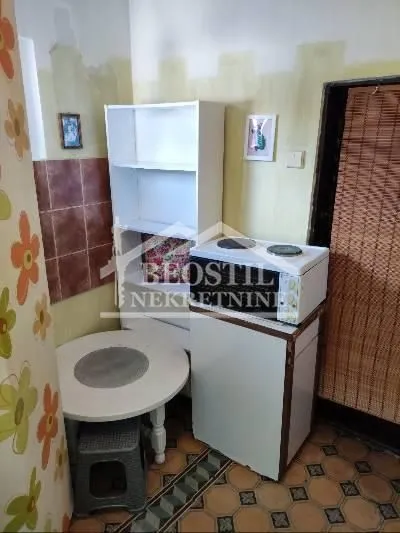Small kitchen with a stove, refrigerator, table, and shelving units.