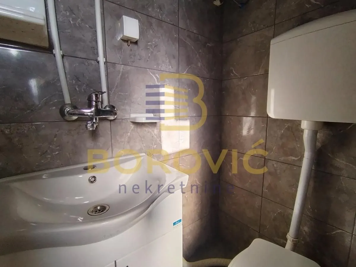 Manje kupatilo obloženo keramičkim pločicama sa umivaonikom i wc šoljom.