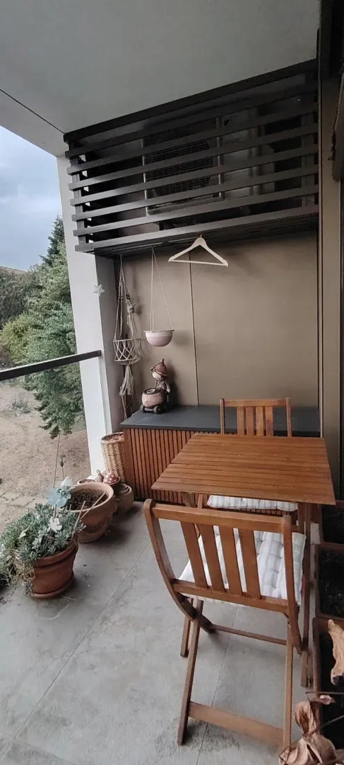 Furnished balcony with a wooden table, chairs, and potted plants.