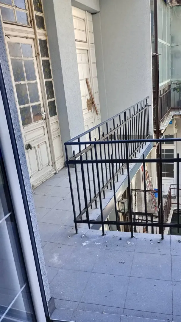 Pogled na spoljašnji balkon sa metalnom ogradom i starim drvenim vratima.