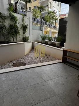 Popločana terasa sa malim uređenim dvorištem i pogledom na zgradu. - image 4