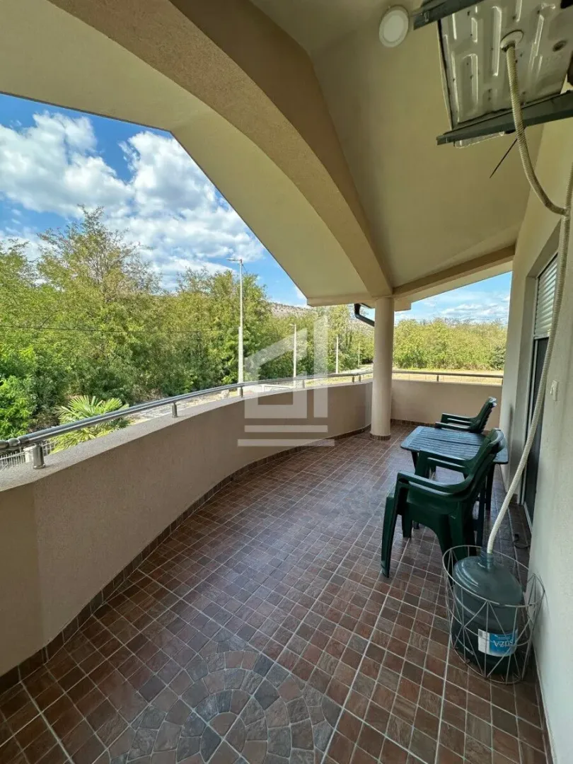 Spacious covered balcony with outdoor seating and a view of greenery.