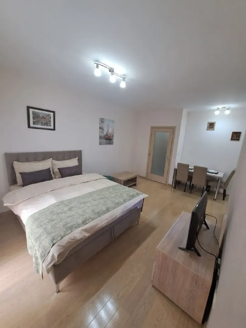 Spacious bedroom with a large double bed, wooden flooring, and a dining area in the background.