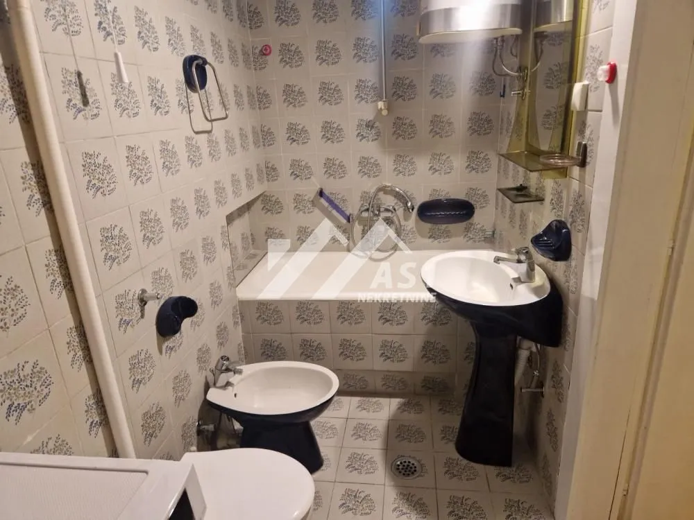Smaller bathroom with a bathtub, washbasin, and sanitary ware tiled with patterned tiles.