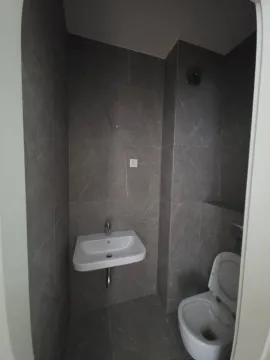 Manje kupatilo sa umivaonikom i šoljom, obloženo sivim pločicama. - image 7