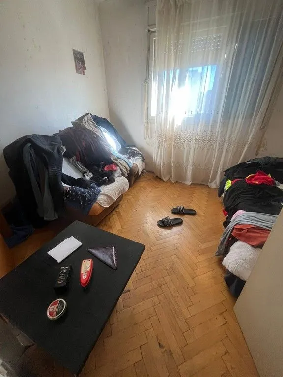 Dnevna soba sa parketom na podu i namještajem zatrpanim garderobom.