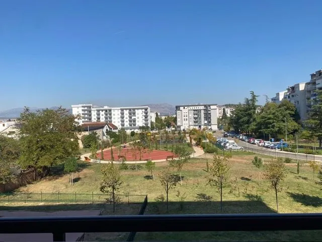 Pogled sa terase na uređeno dvorište i okolne zgrade.