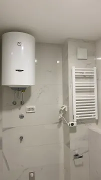 A section of a bathroom showing a water heater and towel radiator on light tiles. - image 10