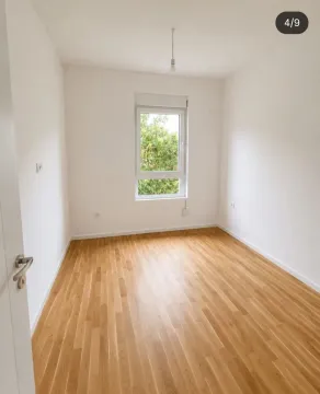 Prazna soba sa bijelim zidovima, drvenim parketom i prozorom. - image 2