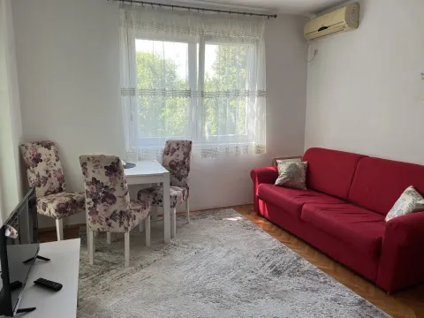 Bright living room with a red sofa, a dining table, and a large window. - image 14