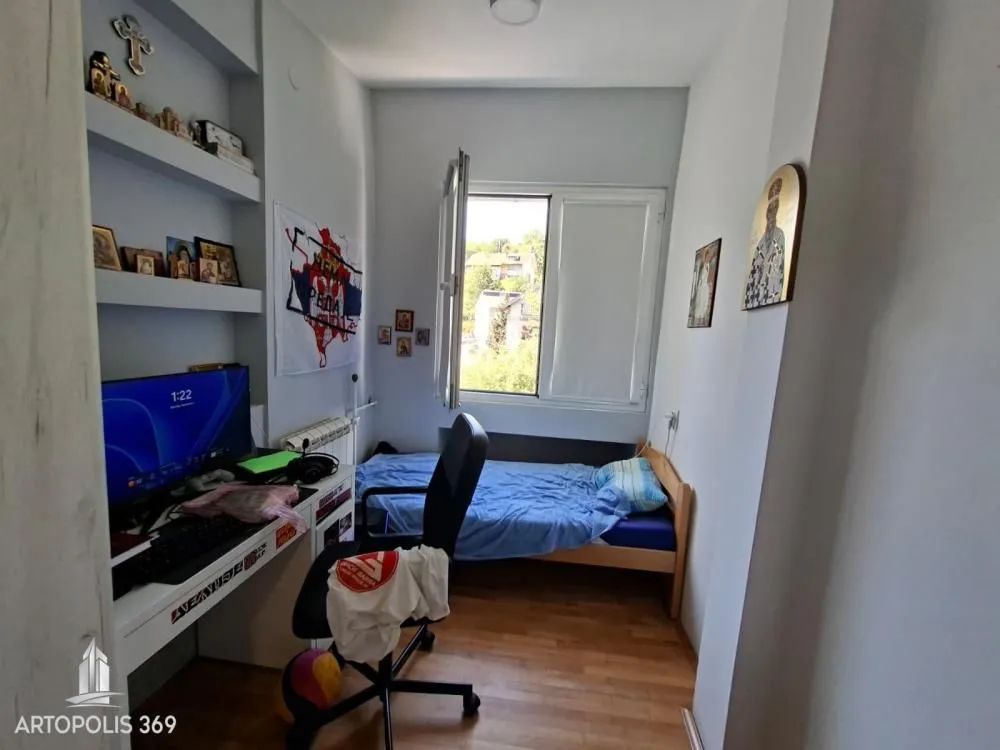 Manja spavaća soba sa krevetom, radnim stolom i računarom.