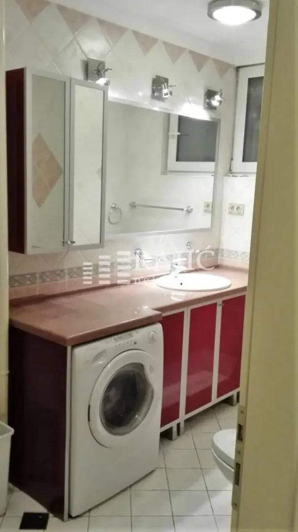 Manje kupatilo sa umivaonikom, ormarićem, ogledalom i veš mašinom.