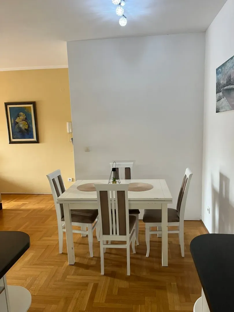 Dining area with a table and white chairs on parquet flooring.