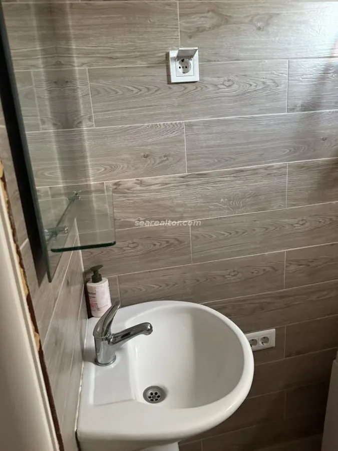 Manje kupatilo sa umivaonikom i zidnim pločicama u dezenu drveta.