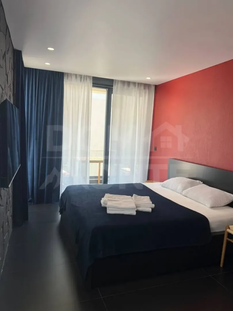 Modern bedroom with a double bed, a red accent wall, and dark flooring.