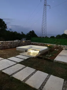 Yard with a paved walkway, illuminated sunken seating area, and stone wall at dusk. - image 9
