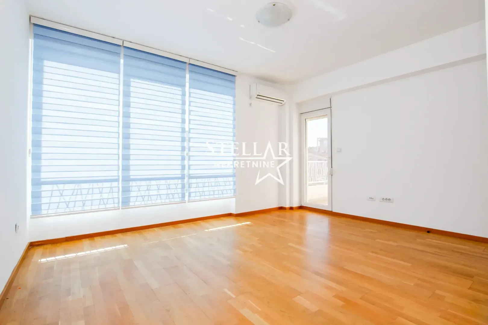 Empty bright room with parquet flooring and large windows.
