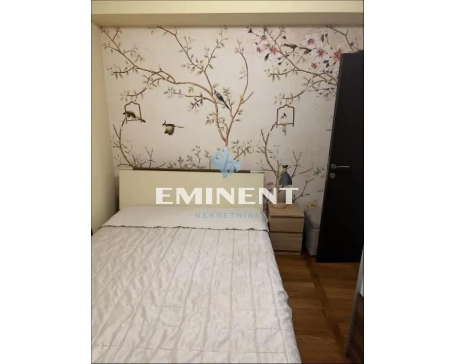 Furnished bedroom with a double bed and decorative wallpaper on the wall.