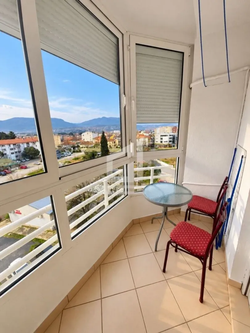 Enclosed balcony with a small table, chairs, and a city view.