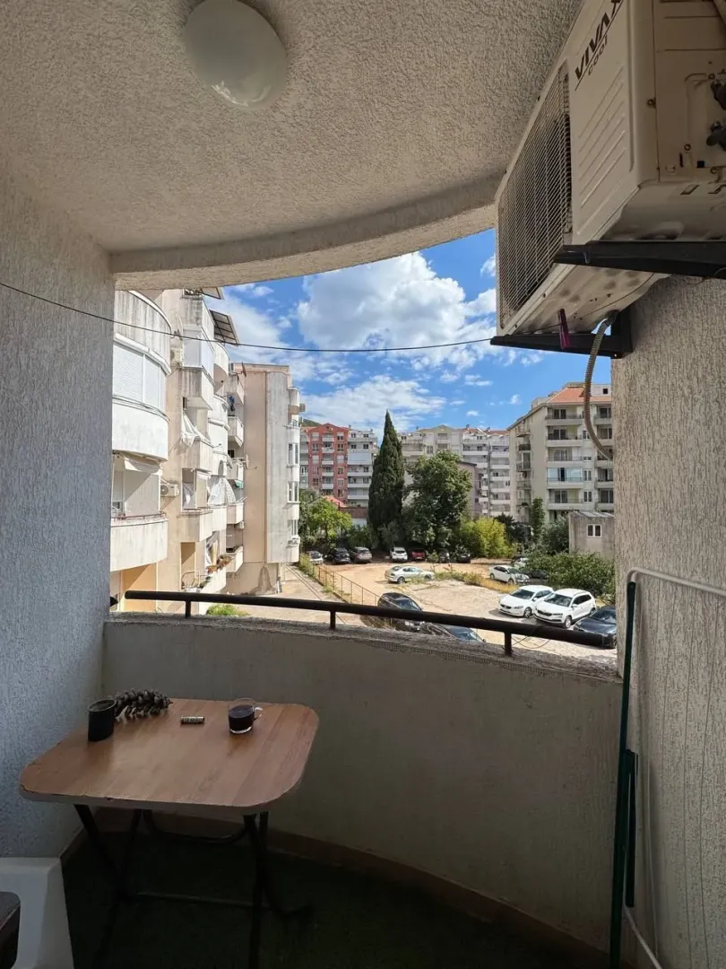 Natkriveni balkon sa stolom i pogledom na zgrade i parking.