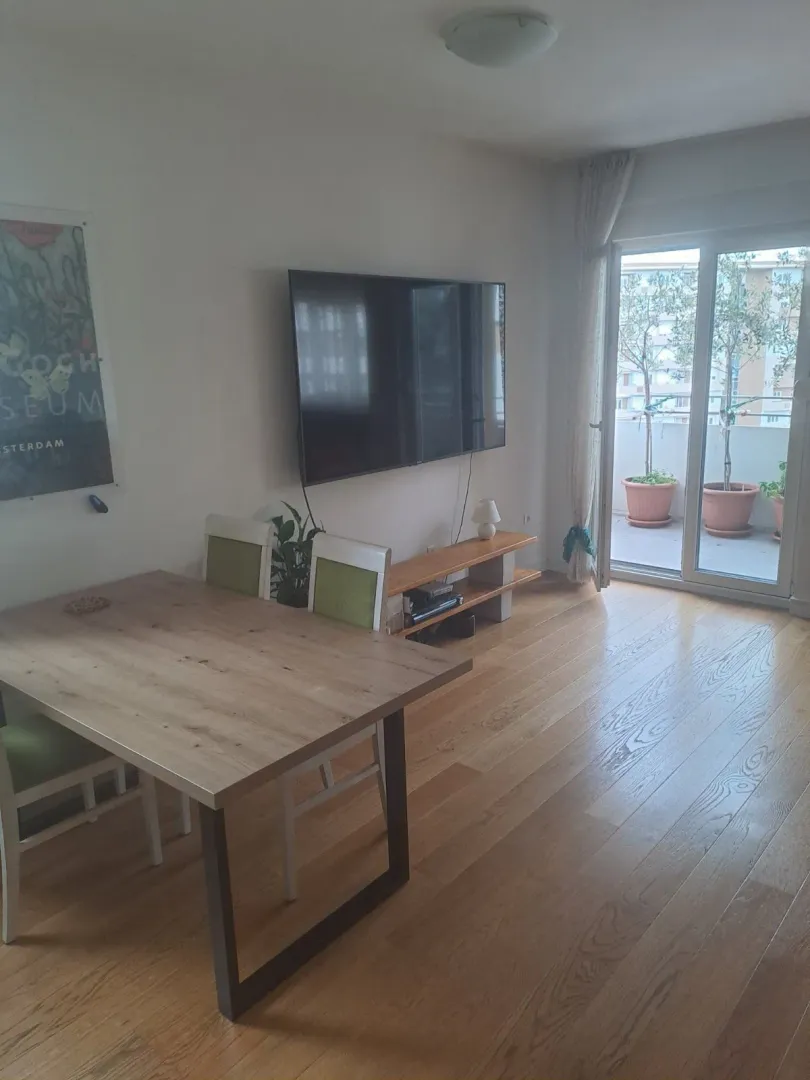 Svijetla dnevna soba sa trpezarijskim stolom, televizorom i izlazom na balkon.