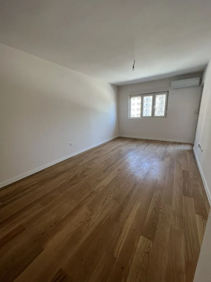 An empty, bright room with wooden flooring and an air conditioning unit.