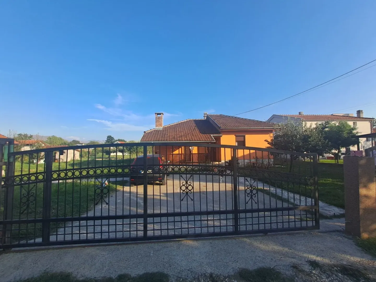 Pogled na dvorište i kuću kroz crnu kovanu kapiju.