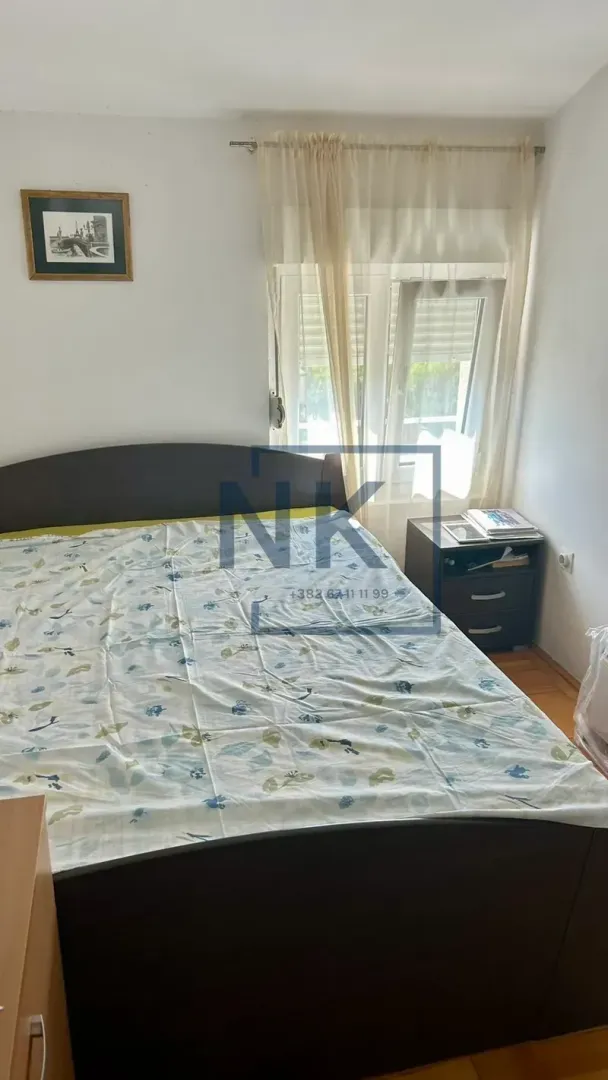 Namještena spavaća soba sa bračnim krevetom, noćnim stočićem i prozorom.