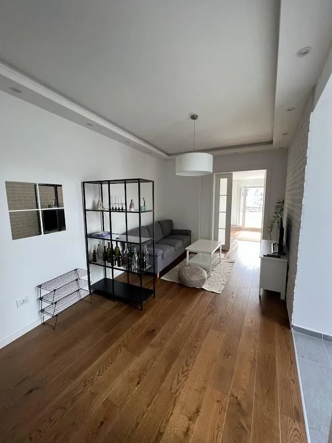 Living room with sofa, shelving unit, and wooden flooring.