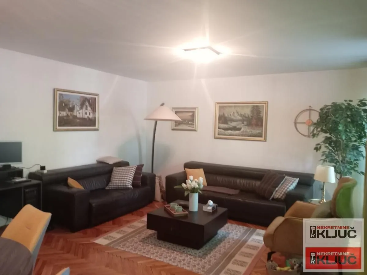 Dnevna soba sa garniturom, stočićem i slikama na zidu.