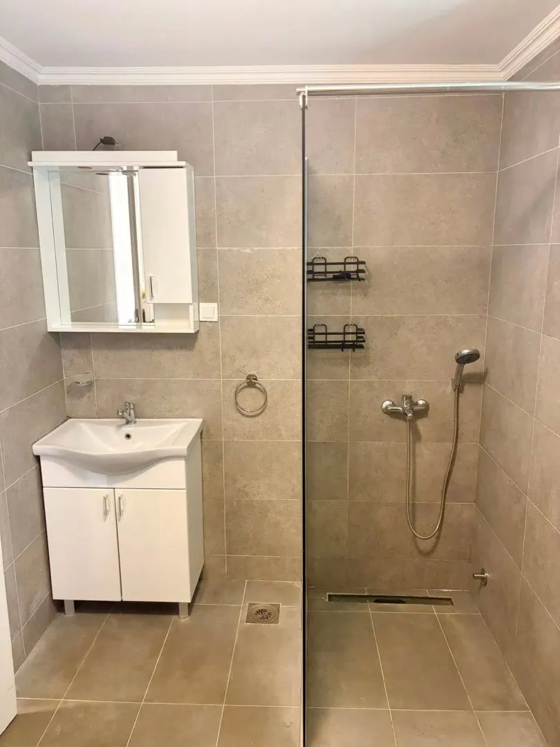 Bathroom tiled in gray with a white sink and a walk-in shower.