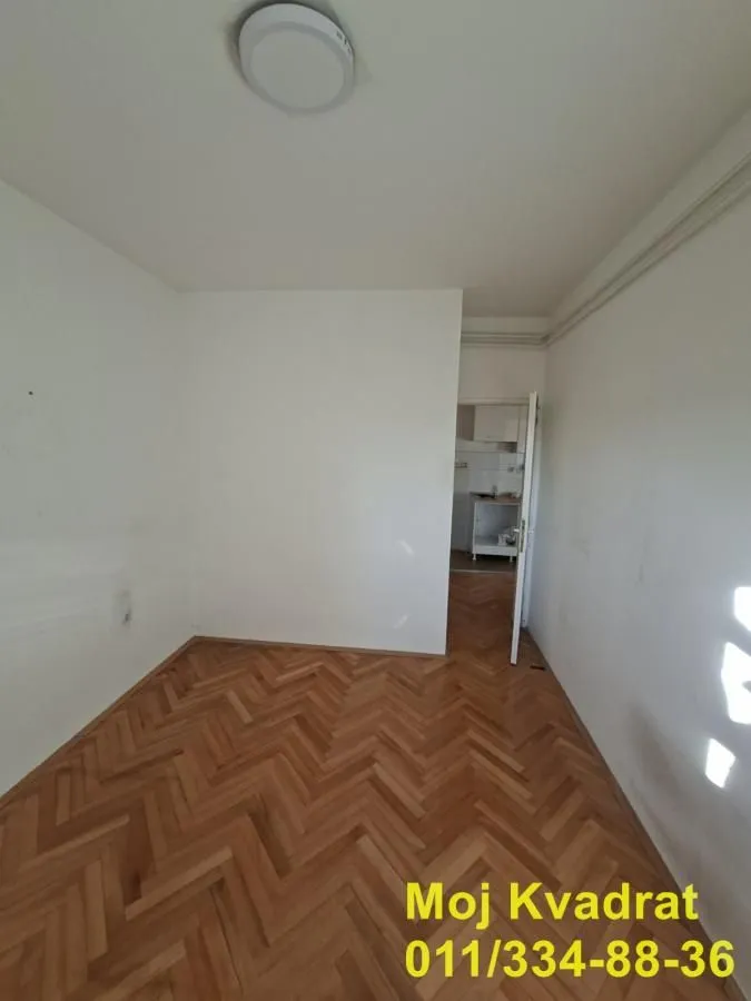 Empty room with parquet flooring and a view into another room through an open door.