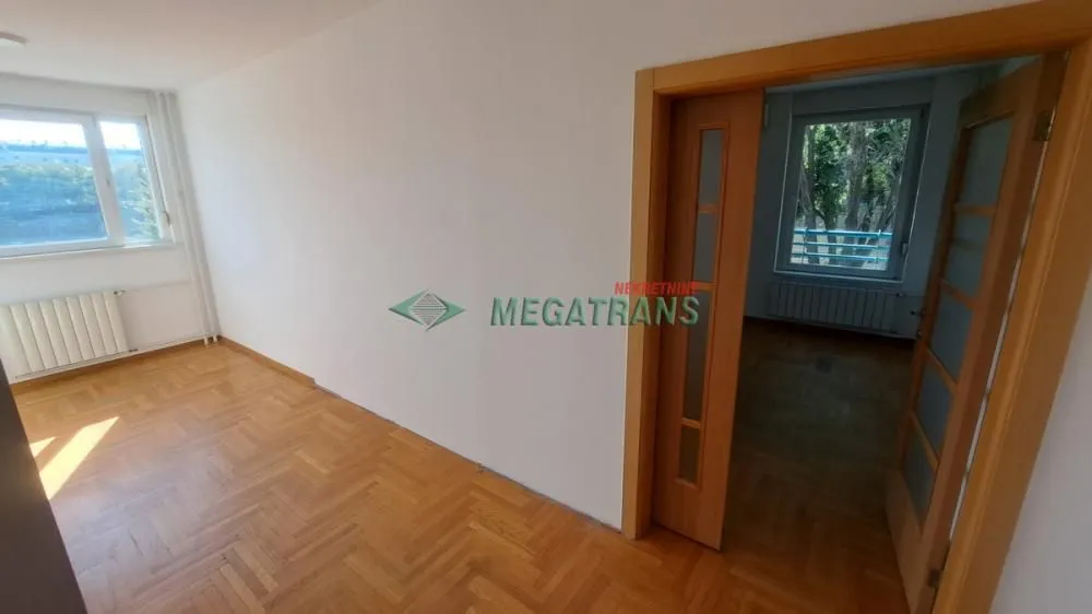 Prazna soba sa parketom i drvenim vratima koja vode u drugu prostoriju.
