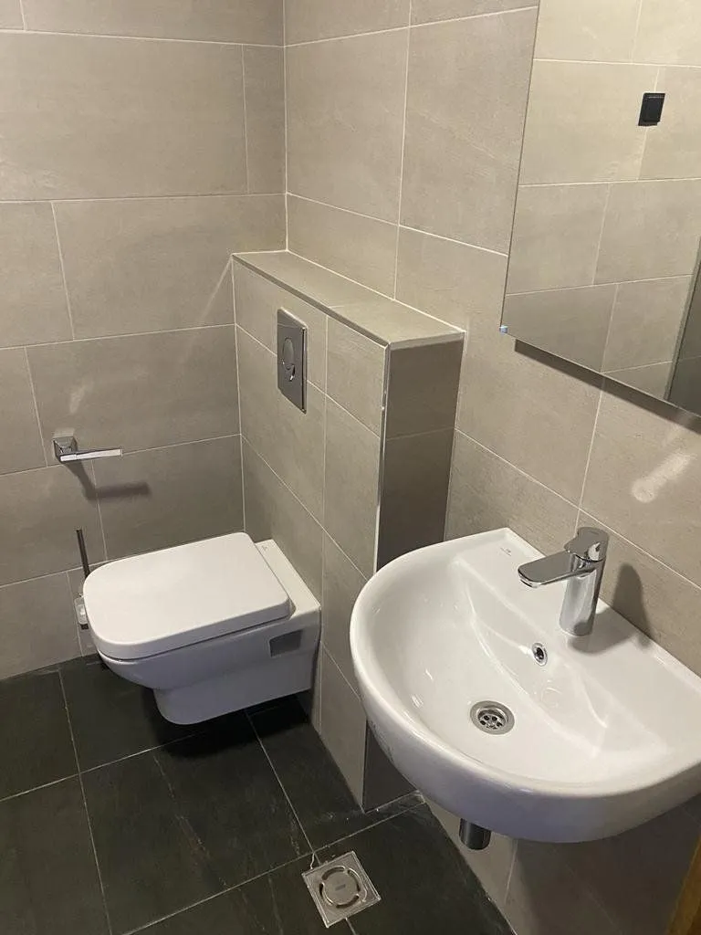 Compact bathroom with neutral-toned tiling, a washbasin, and a toilet.
