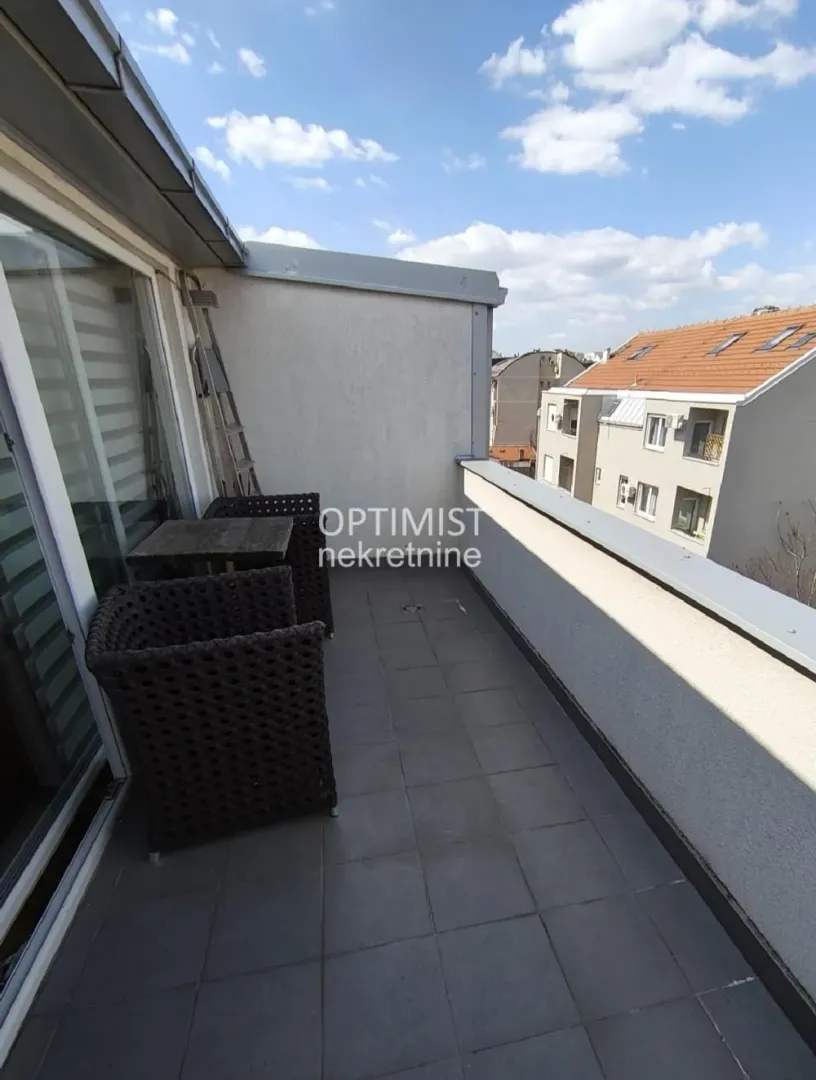 Manji popločani balkon sa garniturom za sedenje i pogledom na okolne zgrade.
