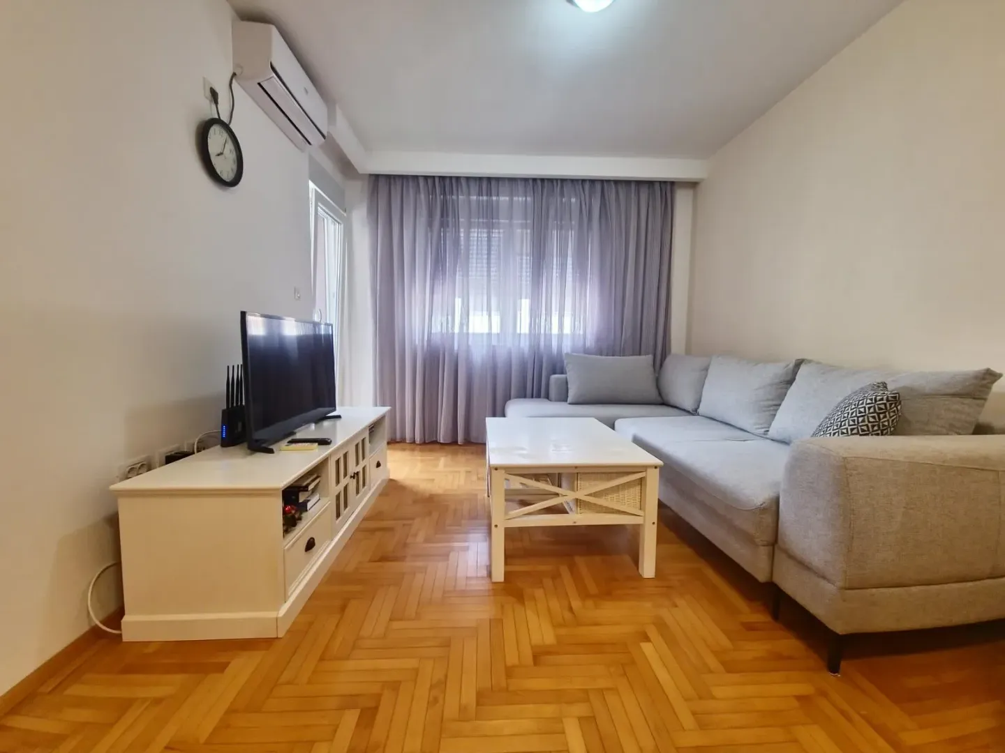 Living room with a sectional sofa, TV unit, and parquet flooring.