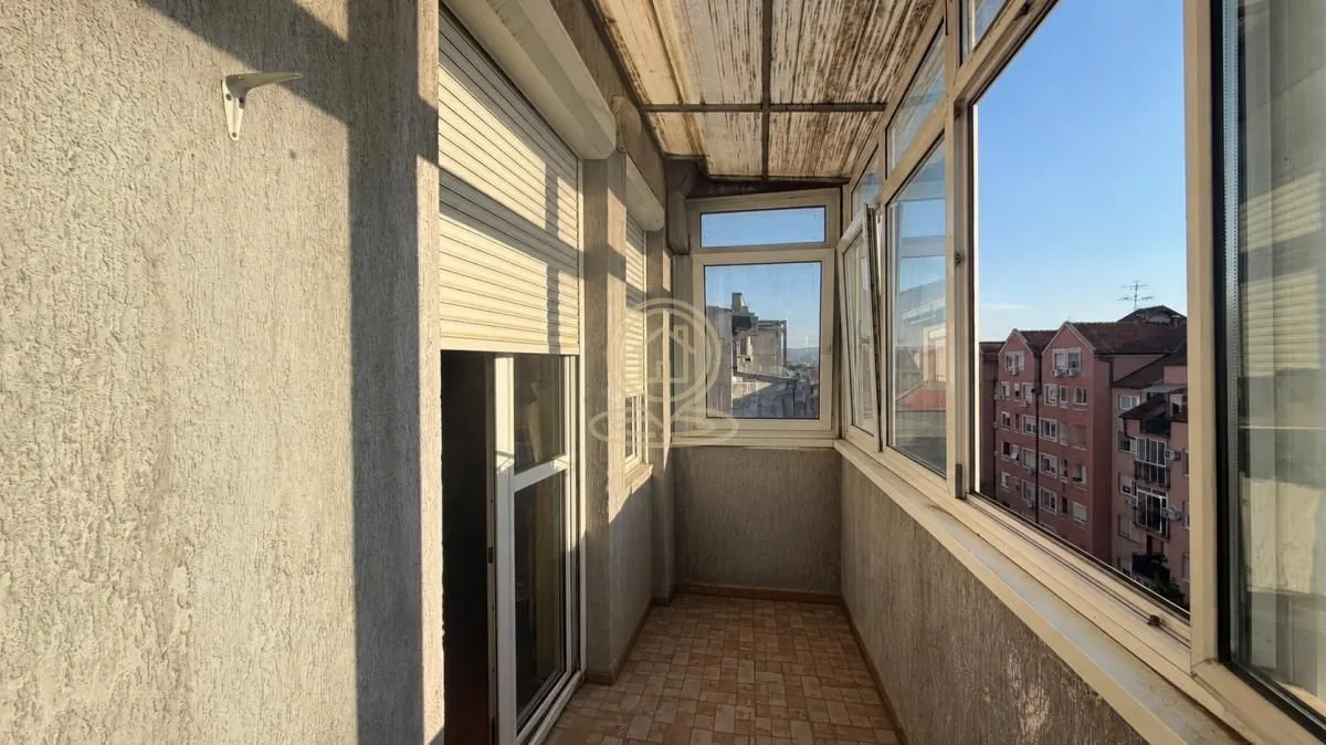Zastakljeni balkon sa pogledom na okolne zgrade.